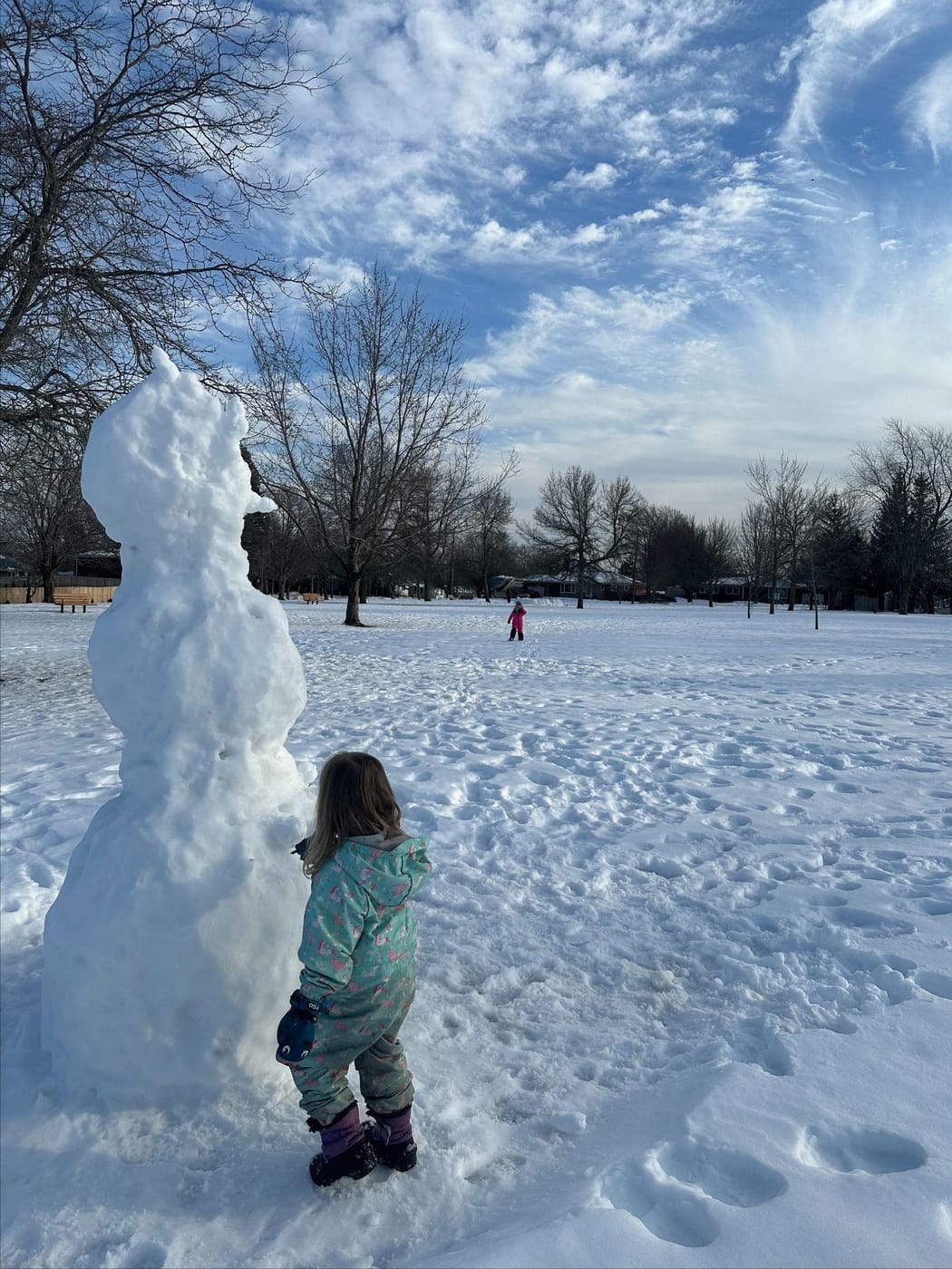 A child beside a tall snowman in a snowy park in New Brunswick
