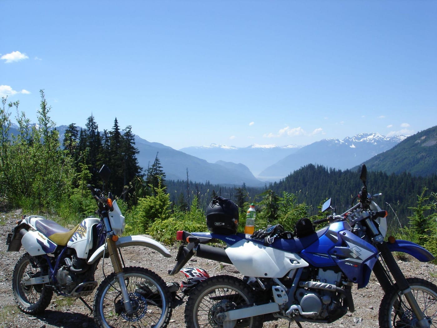 Two Suzuki DR-Z400 motorbikes parked at a mountain lookout above a valley